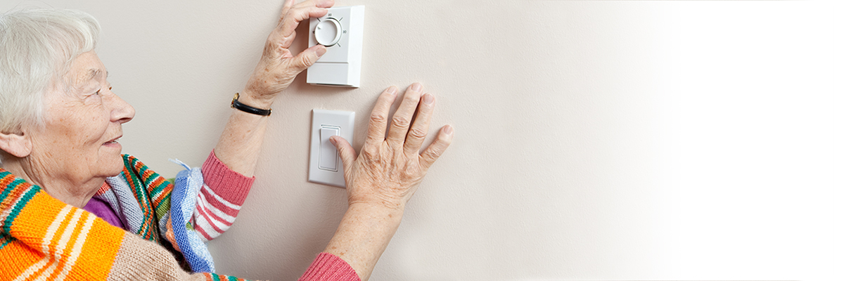 une dame âgée règle le thermostat de son chauffage 